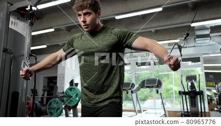Portrait view of the man training arms with trx fitness strips in gym. Sport man with TRX straps spending time in the gym while exercising at the gym. 80965776