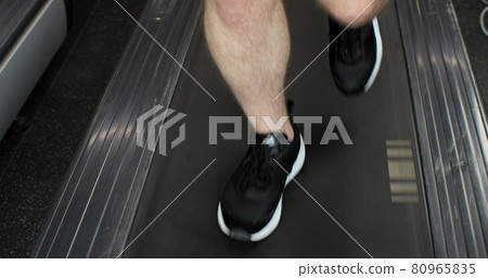 Closeup athletic feet running on treadmill in fitness gym. Front view of shoes having workout on treadmill. Low view sneakers training in sport club. 80965835