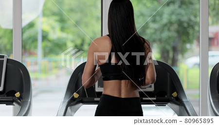 Young fit woman running on treadmill in gym back view. Attractive girl running on the treadmill in the sport gym. Slow Motion. 80965895