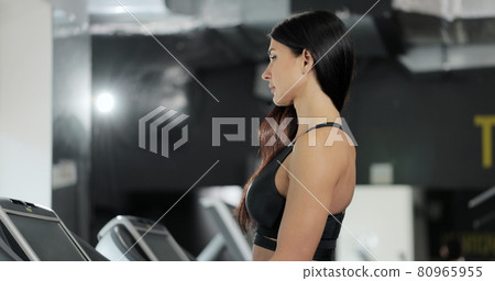 Attractive caucasian girl is starting to run on the treadmill in the sport gym. Portrait of attractive girl athlete training at gym. Sport and healthy lifestyle concept. Attractive caucasian girl is starting to run on the treadmill in the sport gym. Portrait of attractive girl athlete training at gym. Sport and healthy lifestyle concept. 80965955