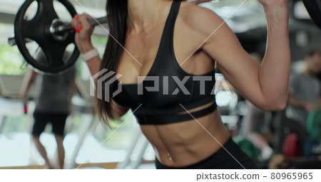 Young fitness beautiful girl lifting a weight cross fit in the gym. Beautiful sporty woman doing squats with barbell enjoying working out. Young fitness beautiful girl lifting a weight cross fit in the gym. Beautiful sporty woman doing squats with barbell enjoying working out. 80965965