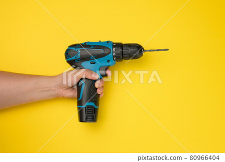 female hand holds a cordless drill on a yellow background. Tool for work 80966404