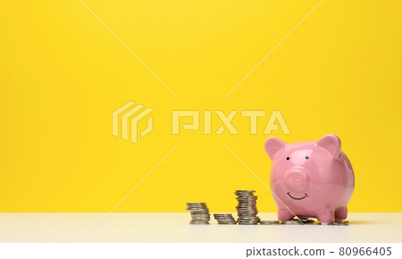 pink ceramic piggy bank and a stack of coins on a white table, yellow background. Savings concept, budget planning 80966405