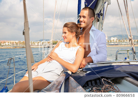 Young woman and man sitting on modern yacht deck, enjoying warm summer day during romantic sea travel Young woman and man sitting on modern yacht deck, enjoying warm summer day during romantic sea travel 80966658