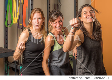 Portrait of three sportswoman showing closed fists in funny way in gym 80968424