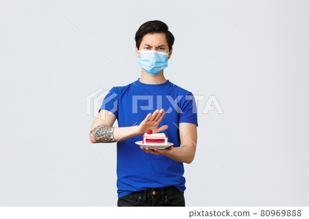 Self-quarantine, home lifestyle and celebration concept. Angry disgusted young asian guy dont like dessert, rejecting awful disgusting cake, frowning disappointed, wear medical mask Self-quarantine, home lifestyle and celebration concept. Angry disgusted young asian guy dont like dessert, rejecting awful disgusting cake, frowning disappointed, wear medical mask 80969888