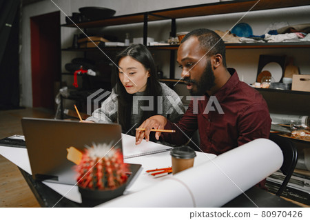 Female tailor and black man doing sketch for clothing in workshop Female tailor and black man doing sketch for clothing in workshop 80970426