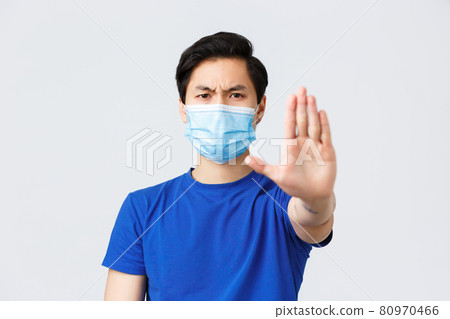 Different emotions, lifestyle and leisure during coronavirus, covid-19 concept. Angry and displeased asian man in medical mask tell to stop with stretched palm, give warning or prohibit something 80970466