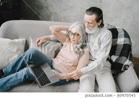 Senior couple sitting on couch with laptop 80970545
