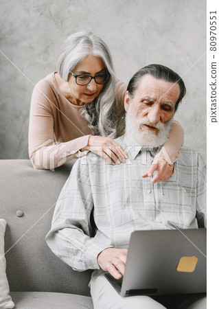 Senior couple sitting on couch with laptop 80970551