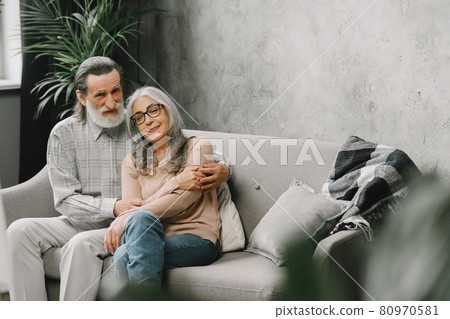 Senior couple in casual clothes sitting on couch in living room 80970581