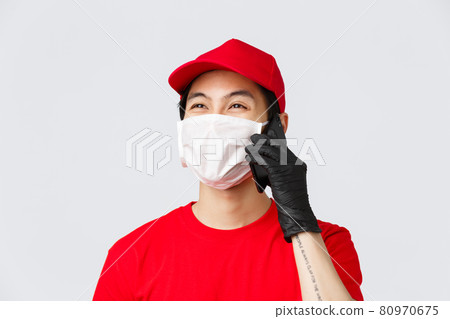 Covid-19, self-quarantine online shopping and delivery concept. Friendly young asian courier in medical mask and protective gloves, calling client, answer customer phonecall, smiling, grey background Covid-19, self-quarantine online shopping and delivery concept. Friendly young asian courier in medical mask and protective gloves, calling client, answer customer phonecall, smiling, grey background 80970675