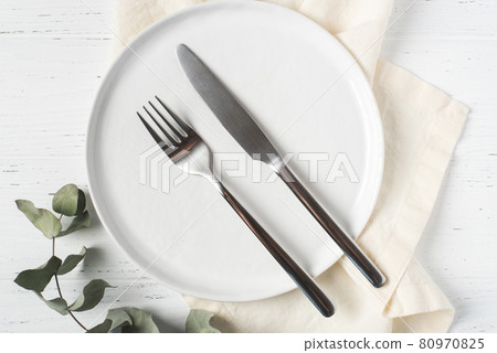 An empty plate and cutlery on a white table. 80970825