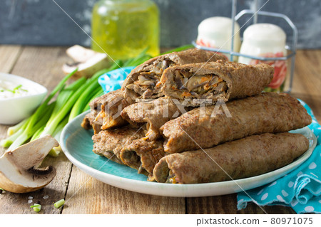 The concept of a healthy breakfast or snack. Meat liver pancakes stuffed with mushrooms and vegetables in a plate on rustic wooden table. 80971075