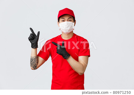 Upset, disappointed asian courier complaining about advertisement. Delivery man in red t-shirt and cap, wearing medical mask and protective gloves during covid19, pointing fingers upper left corner 80971250