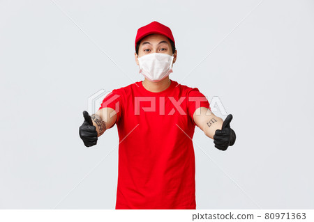 Cheerful smiling asian courier in red cap and t-shirt stretch hands forward to take parcel from client at delivery company. Deliver guy in uniform, medical mask and gloves receive shipping goods 80971363