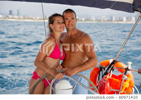 Couple standing at yacht wheel along coast of Barcelona 80971410