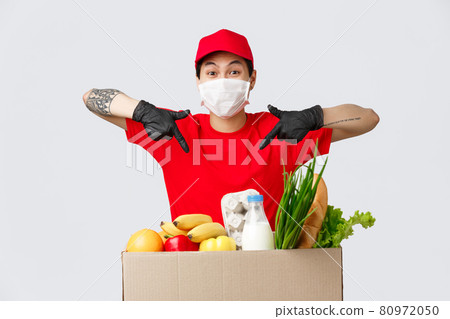 Online shopping, food delivery and coronavirus concept. Smiling asian courier pointing fingers at package with fresh groceries, deliver goods to client home during quarantine, customer online order Online shopping, food delivery and coronavirus concept. Smiling asian courier pointing fingers at package with fresh groceries, deliver goods to client home during quarantine, customer online order 80972050