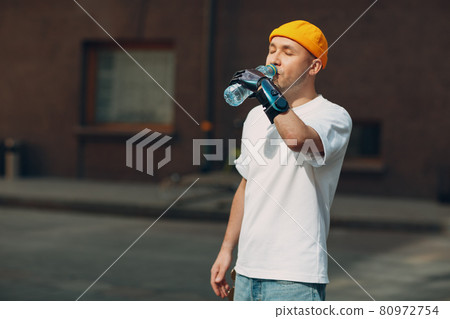 Young disabled man hold and drink bottled pure water with artificial prosthetic hand in casual clothes. 80972754
