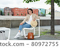 Happy young woman is resting on a bench on the embankment of the Moscow River in summer and smiling. 80972755