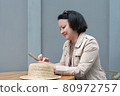Smiling woman sits at a table in a cafe and writes messages on the phone. 80972757