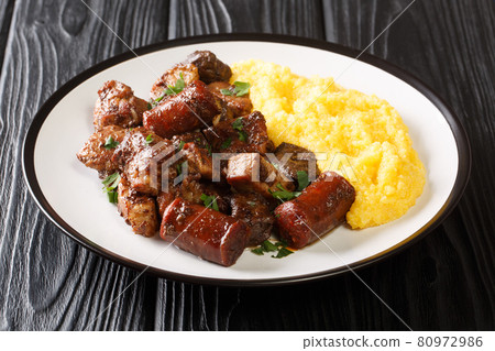 Delicious fried pork, sausages and offal with garlic served with corn porridge close-up in a plate. horizontal 80972986
