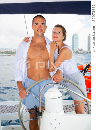 Woman and man steering yacht along shoreline of Spain Woman and man steering yacht along shoreline of Spain 80973451