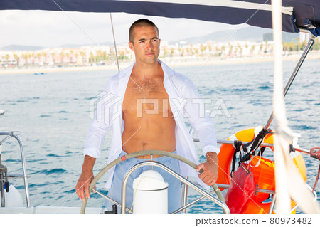 Man steering yacht along Barcelona coastline 80973482