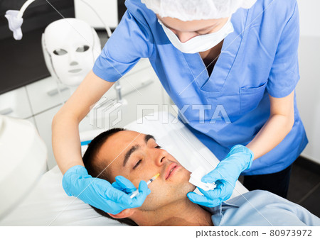 Man receiving injections for facial contouring in cosmetology clinic Man receiving injections for facial contouring in cosmetology clinic 80973972