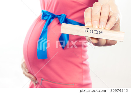Woman in pregnant wearing pink dress with blue ribbon and showing word june Woman in pregnant wearing pink dress with blue ribbon and showing word june 80974343