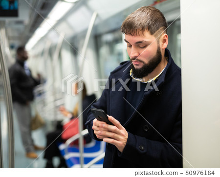 Young man with phone in metro car Young man with phone in metro car 80976184