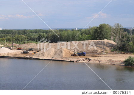 Loading soil onto trucks on a river jetty, heaps of gravel on the river bank, construction 80976354
