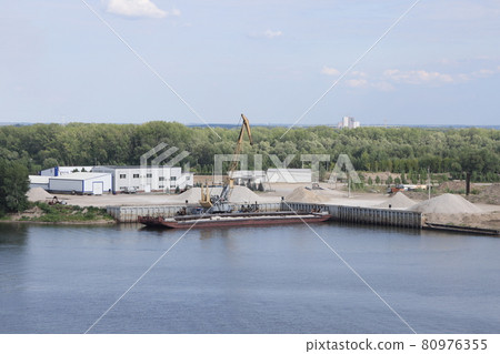Unloading a barge in a river port, gantry crane unloading crushed stone, river background Unloading a barge in a river port, gantry crane unloading crushed stone, river background 80976355