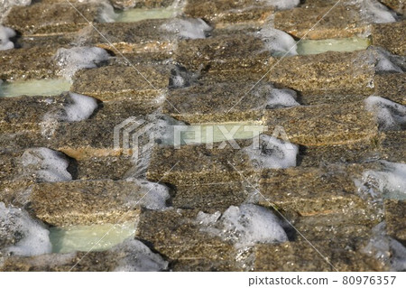 Water flows down a granite grate, foam stream, a fragment of a fountain, granite background 80976357