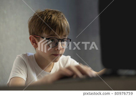 Boy in glasses enthusiastically plays computer games. Teen boy is studying online. Preparing to exams Boy in glasses enthusiastically plays computer games. Teen boy is studying online. Preparing to exams 80976759
