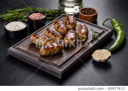 Grilled sausage with the addition of herbs and vegetables on the dark background Grilled sausage with the addition of herbs and vegetables on the dark background 80977613