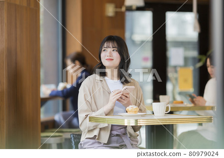 在一家咖啡館經營智能手機的年輕女子 80979024