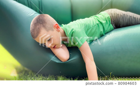 Portrait of a caucasian boy 7 years old in a green t-shirt resting on a lamzak, inflatable lounger. Portrait of a caucasian boy 7 years old in a green t-shirt resting on a lamzak, inflatable lounger. 80984603