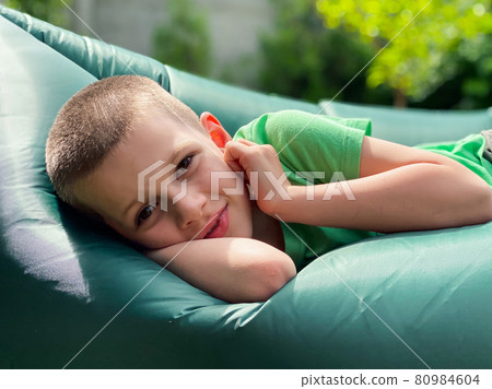 Portrait of a caucasian boy 7 years old in a green t-shirt resting on a lamzak, inflatable lounger. Portrait of a caucasian boy 7 years old in a green t-shirt resting on a lamzak, inflatable lounger. 80984604