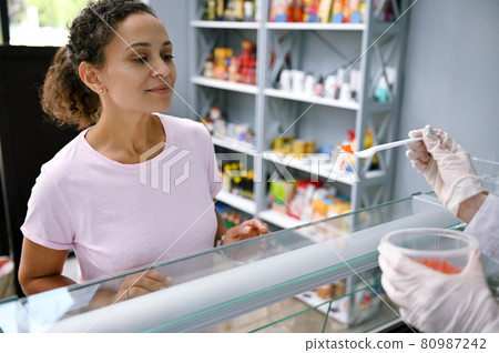 Cropped fishmonger standing behind the counter, holding a jar with red salmon caviar and serving the customer, offering to taste the seafood delicacy Cropped fishmonger standing behind the counter, holding a jar with red salmon caviar and serving the customer, offering to taste the seafood delicacy 80987242