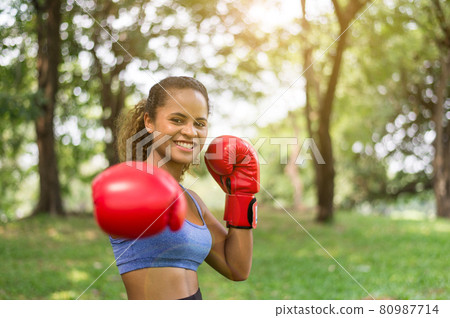 Fit black woman boxer punching at park,Female boxer eye looking training to camera Fit black woman boxer punching at park,Female boxer eye looking training to camera 80987714