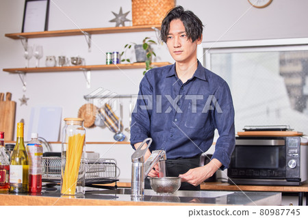Image of a young man cooking in an apron cooking in the kitchen 80987745