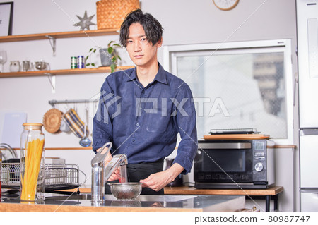 Image of a young man cooking in an apron cooking in the kitchen Image of a young man cooking in an apron cooking in the kitchen 80987747