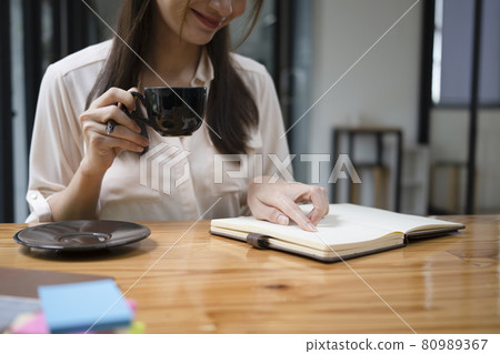 Smiling young woman drinking hot coffee and reading book at home. Smiling young woman drinking hot coffee and reading book at home. 80989367