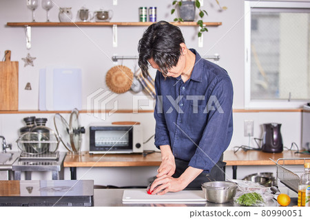 A young man in an apron who cuts tomatoes with a kitchen knife. A young man in an apron who cuts tomatoes with a kitchen knife. 80990051