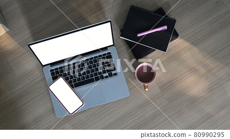 Top view of  simple workspace with blank screen laptop, mobile phone, coffee cup and notebook on wooden table. 80990295