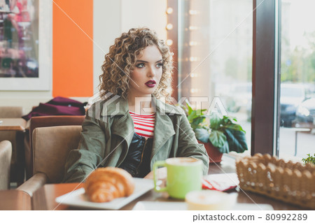 Young anxious woman looking at window in city street cafe 80992289
