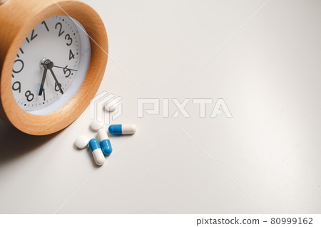 Alarm clock and white blue pills on white table background 80999162