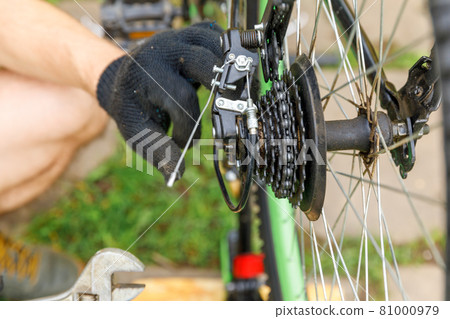 Bike mechanic man repairs bicycle in bicycle repair shop, outdoor. Hand of cyclist bicyclist examines, fixes modern cycle transmission system. Bike maintenance, sport shop concept. Bike mechanic man repairs bicycle in bicycle repair shop, outdoor. Hand of cyclist bicyclist examines, fixes modern cycle transmission system. Bike maintenance, sport shop concept. 81000979