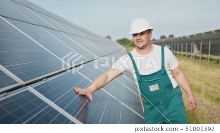 Portrait of proud worker industrial engineer in uniform standing on field with large solar batteries. Ecological farm. Solar power station. People. Sustainable energy. Solar power field. Ecology. Portrait of proud worker industrial engineer in uniform standing on field with large solar batteries. Ecological farm. Solar power station. People. Sustainable energy. Solar power field. Ecology. 81001392
